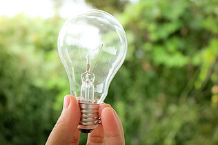 Hand holding a light bulb in front of a green background.