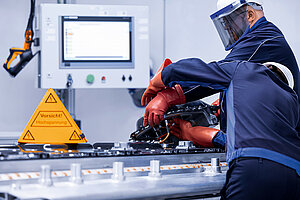 Two Leadec employees in protective clothing repairing a defective battery, on the left-hand a warning sign for working under high voltage.