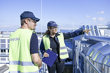 Zwei Leadec-Mitarbeitende bei der Inspektion von Rohrleitungen auf einem Fabrikdach.