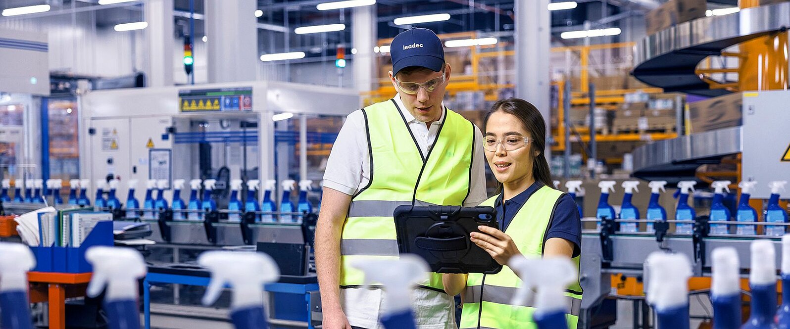 Ein männlicher und ein weiblicher Leadec-Mitarbeiter schauen auf ein Tablet und überwachen die Produktion von Reinigungsmitteln.