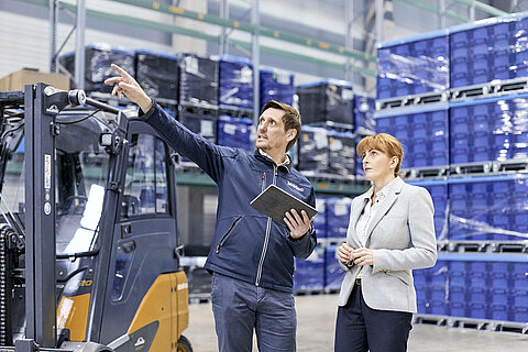 A Leadec employee with a tablet is showing something to a customer in a warehouse.