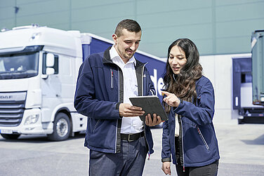 Ein männlicher und ein weiblicher Leadec-Mitarbeiter stehen vor einem Lastwagen und schauen auf ein Tablet.