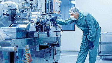 Man in protective clothing stands at a machine and inspects it.