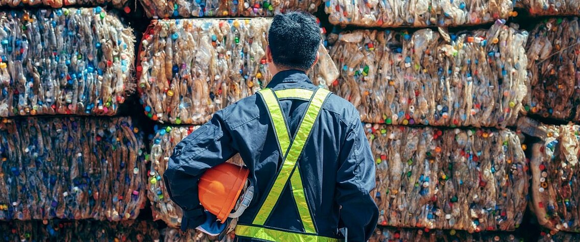 Man in work clothes standing in front of a pile of garbage.