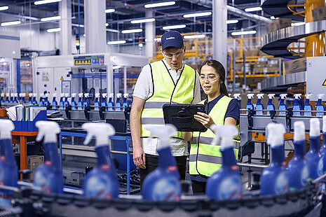 Ein männlicher und ein weiblicher Leadec-Mitarbeiter schauen auf ein Tablet und überwachen die Produktion von Reinigungsmitteln.