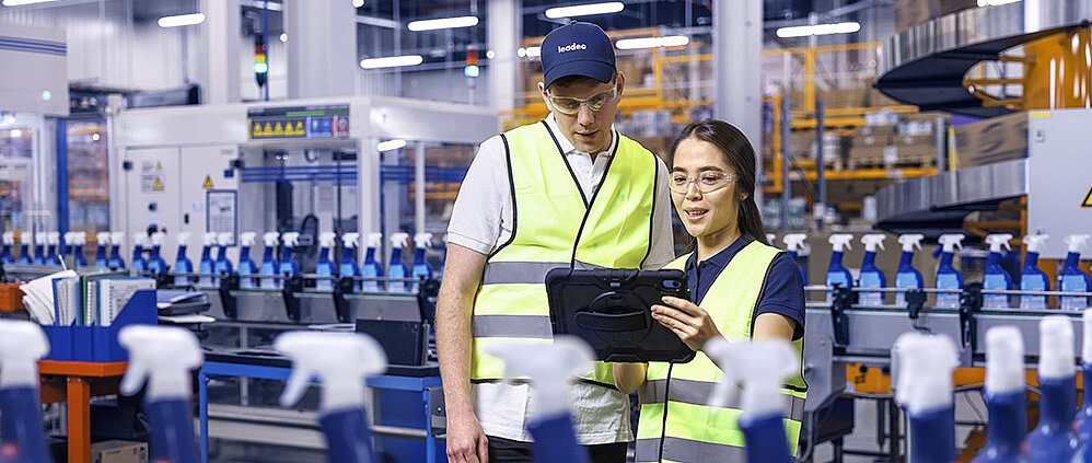 Ein männlicher und ein weiblicher Leadec-Mitarbeiter schauen auf ein Tablet und überwachen die Produktion von Reinigungsmitteln.