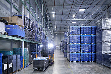 A Leadec employee driving forklift with small load carriers through a warehouse.