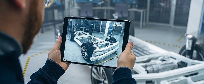 Person with tablet in hand, in the background the basic structure of an electric vehicle. 