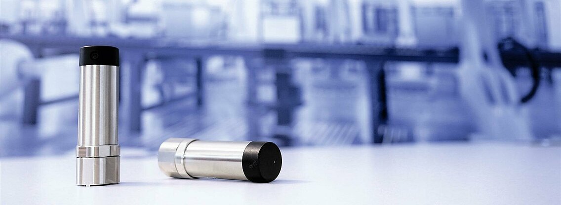 Two vibration sensors in front of a blurred factory background. 