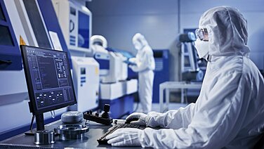 Menschen in einem Reinraum mit Schutzkleidung am Computer. 