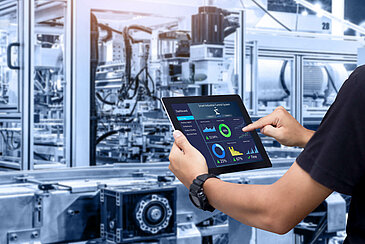 Employee with tablet in hand checks the performance of a machine.