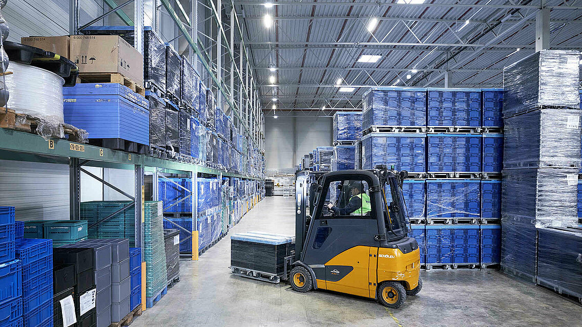 A Leadec employee driving a forklift with small load carriers through a warehouse.