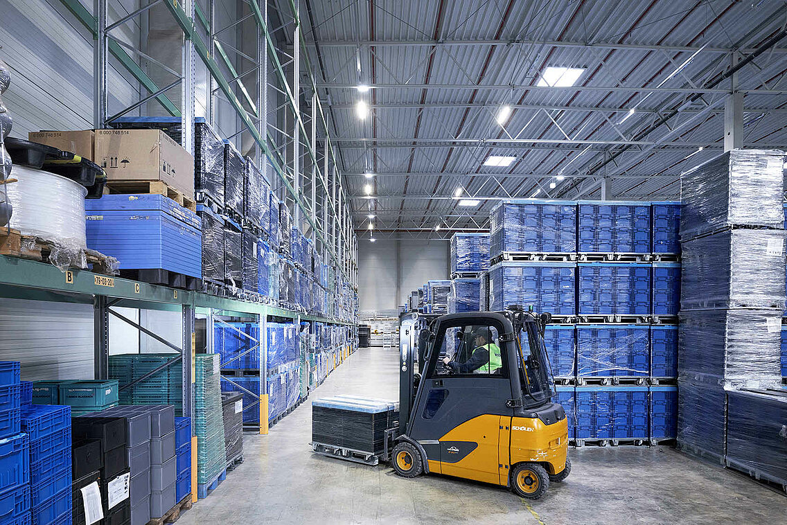 A Leadec employee driving a forklift with small load carriers through a warehouse.