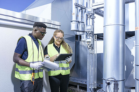 Two Leadec employees with check list and tablet at ventilation system on a factory roof.