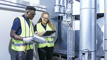 Two Leadec employees with check list and tablet at ventilation system on a factory roof.