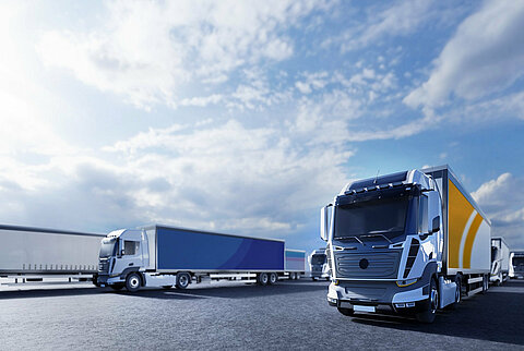 Several buses and trucks are parked together on an asphalt surface.