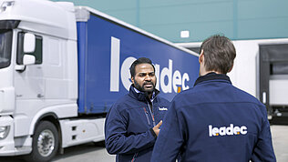 Two male Leadec employees talking in front of a truck.