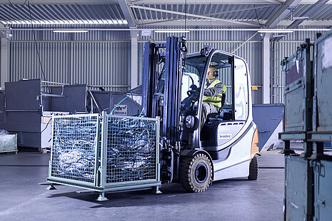 A Leadec employee driving with a forklift with a pallet of waste through factory.