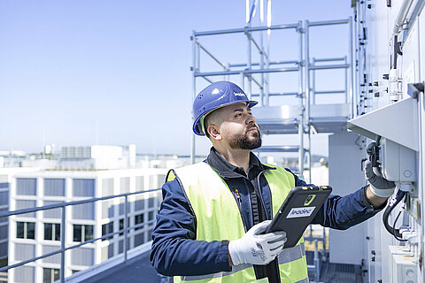 Leadec employee with tablet on a factory roof checks external installation of ventilation system.