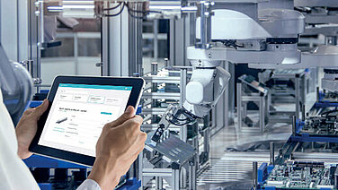 Man holds tablet in front of a system and checks stock of spare parts.