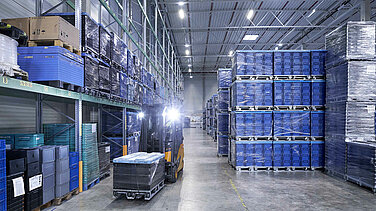 A Leadec employee driving forklift with small load carriers through a warehouse.