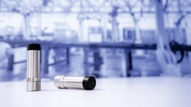 Two vibration sensors in front of a blurred factory background.