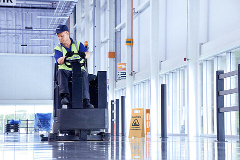 A Leadec employee cleaning the floor at a factory with a cleaning machine.