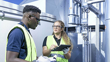 Two Leadec employees with check list and tablet at ventilation system on a factory roof.