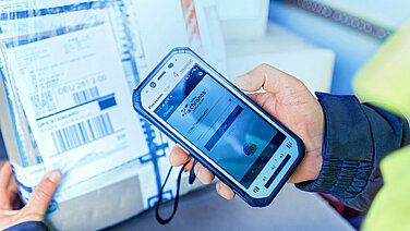 Close-up of a hand with a scanner, on the left a parcel.