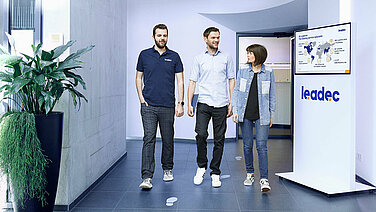 Three Leadec employees walking through the entrance area of the Leadec office in Stuttgart.