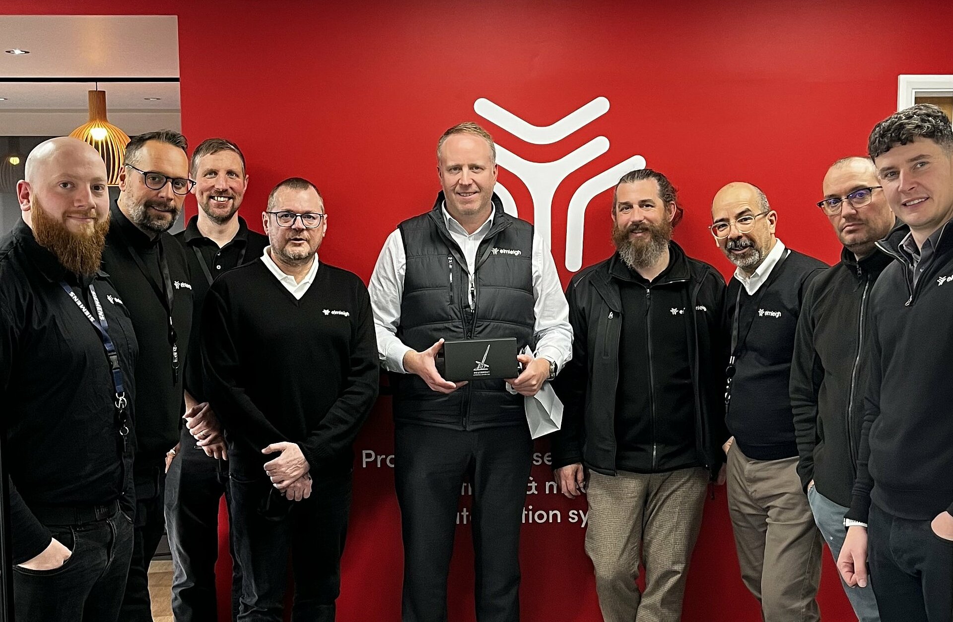 A team of 9 Elmleigh employees in front of the company logo
