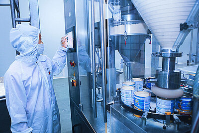 Person in protective clothing standing at a food processing machine.